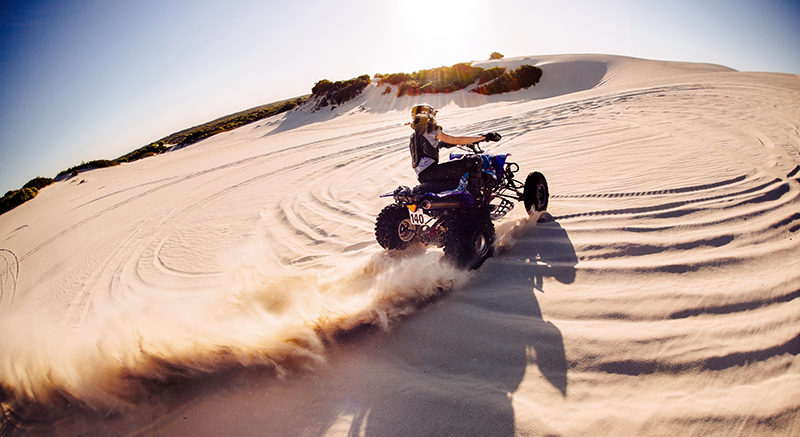 Professional quad biker kicking up sand on a dune